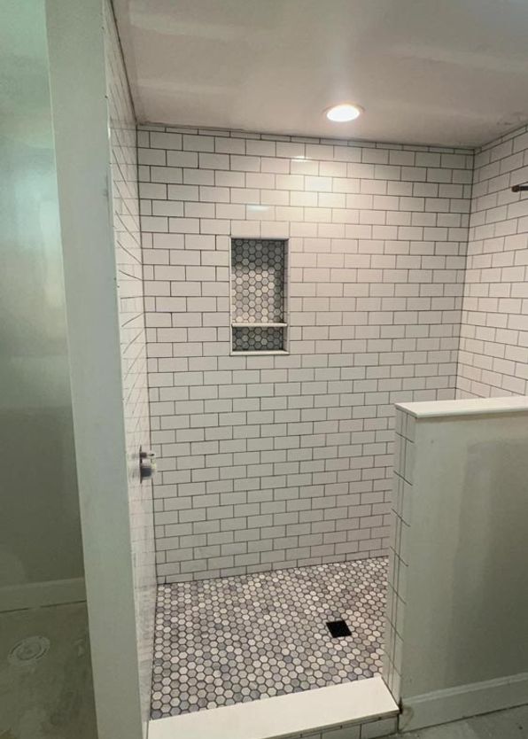 White subway tile shower with hexagonal mosaic floor and recessed niche