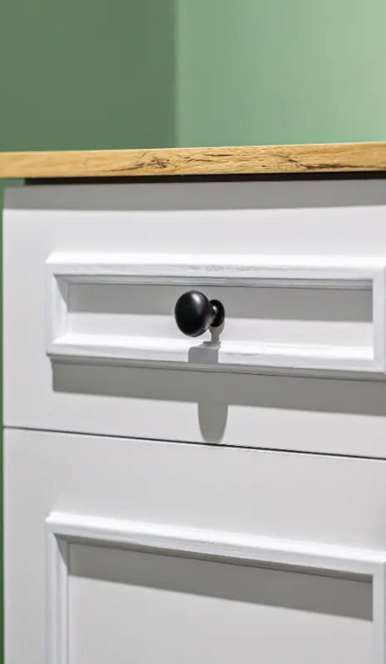 Freshly painted white cabinet with black knobs against a green wall