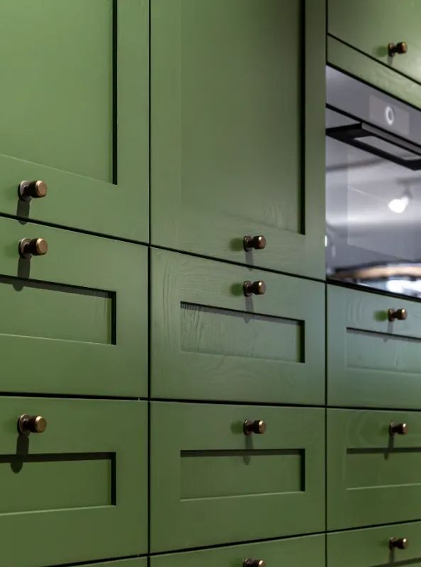Close-up of large green-painted kitchen cabinets with brass knobs