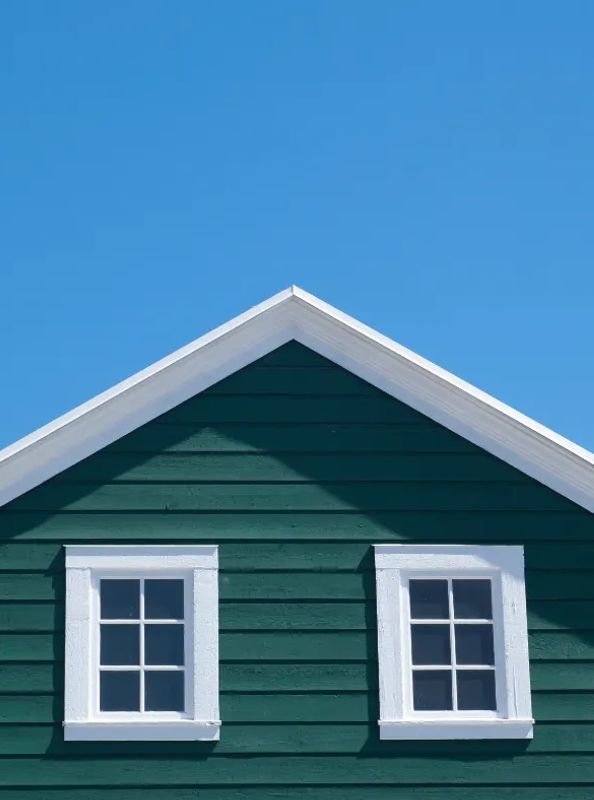 Green-sided home with crisp white roof gable against blue sky