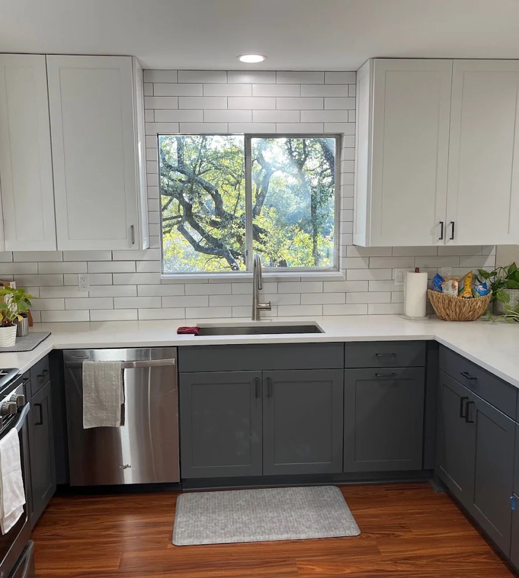 Bright remodeled kitchen with white upper cabinets, gray lower cabinets, white subway backsplash, and hardwood floors